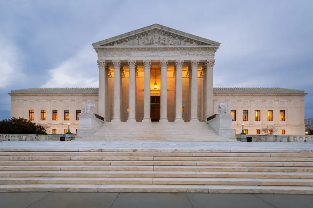Detailed view of the U.S. Supreme Court building under a clear sky with the Constitution and a modern AR-15 rifle subtly overlaid in the foreground